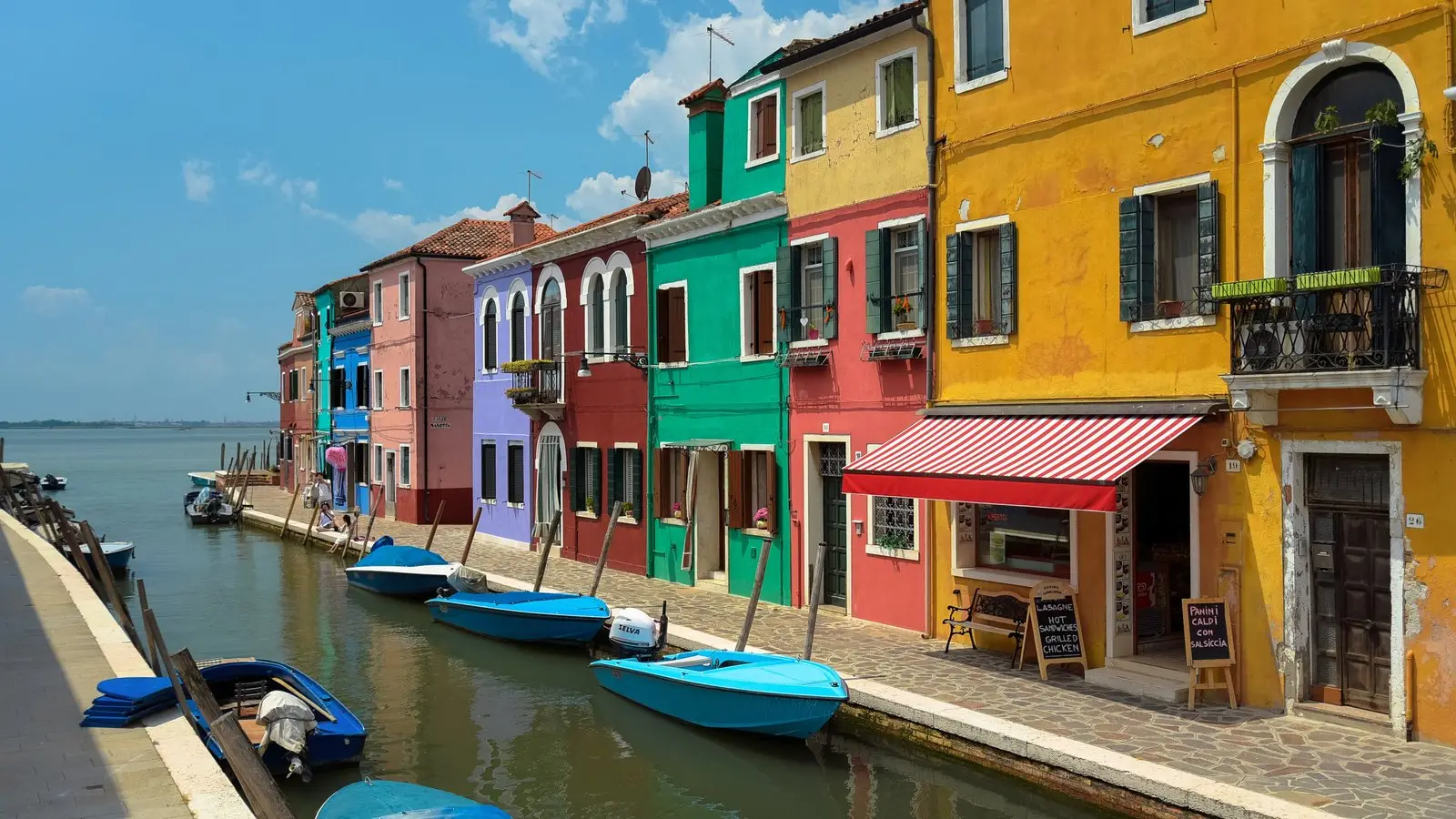 Vibrant rainbow-hued fishermen cottages reflecting across mirror-still canal waters in Burano.