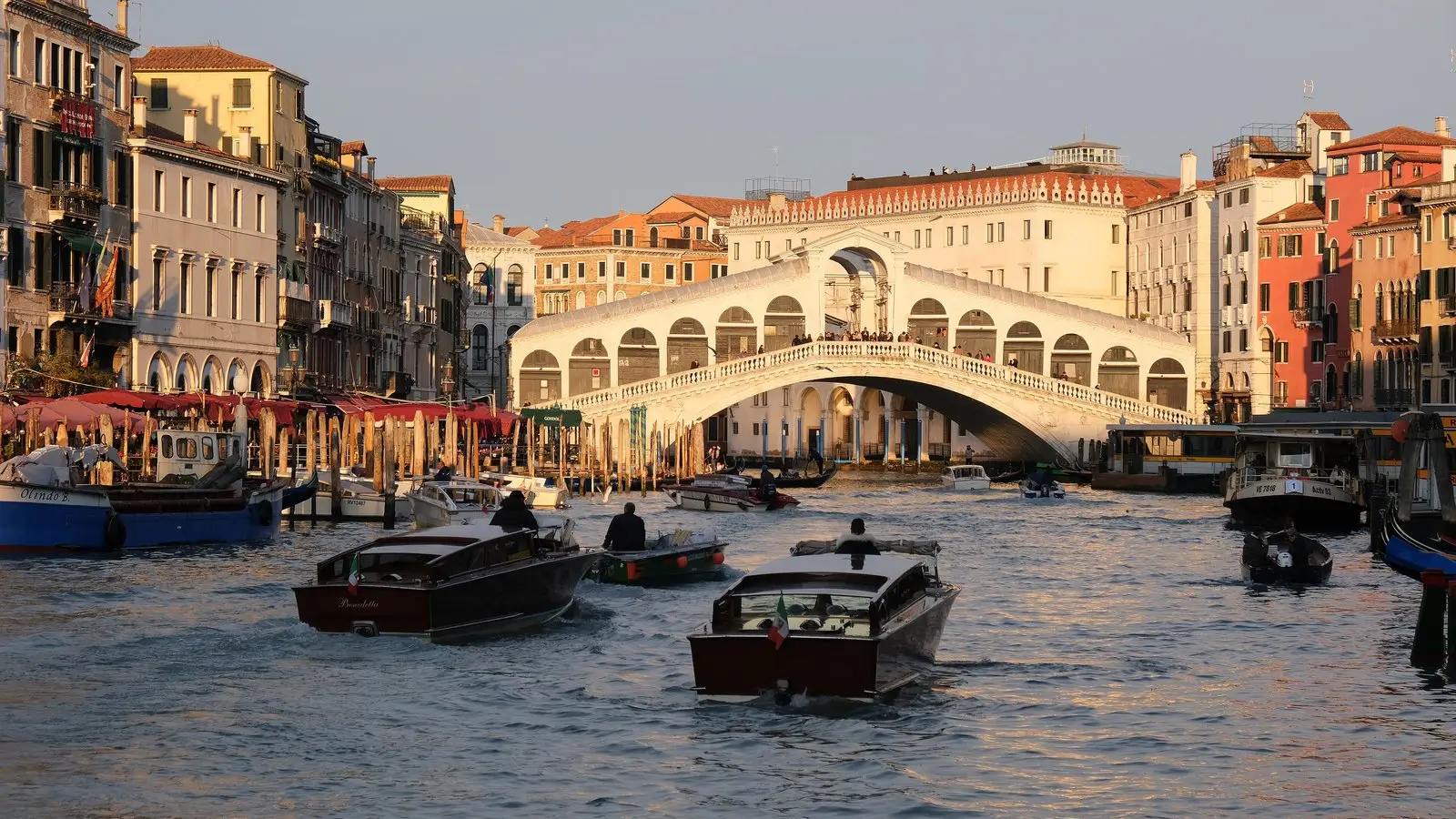 The grand stone arch of Rialto Bridge spanning across busy water traffic along Venice's Grand Canal.